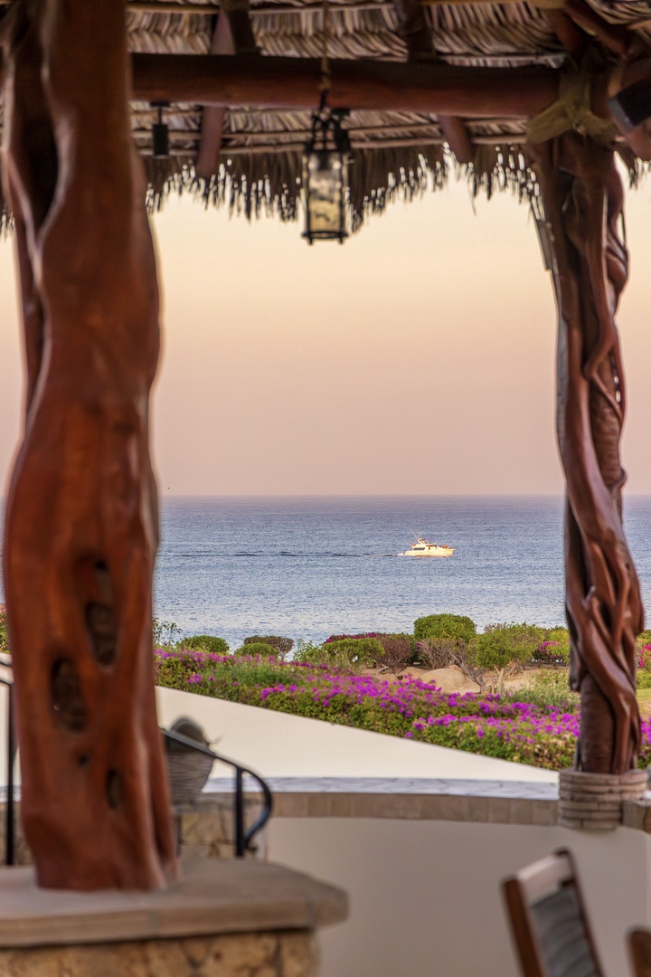 Gaze through carved wooden pillars to endless sea views framed by vibrant bougainvillea—your peaceful haven where tranquil waters meet coastal beauty.