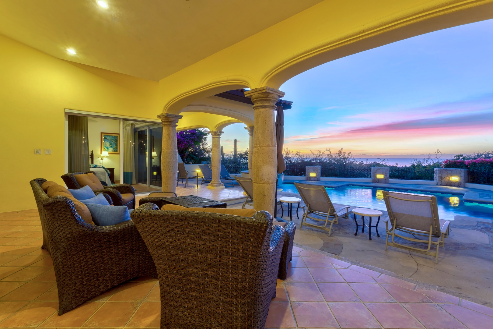 Relax in your covered patio sanctuary with plush seating overlooking the shimmering pool as twilight paints the sky.