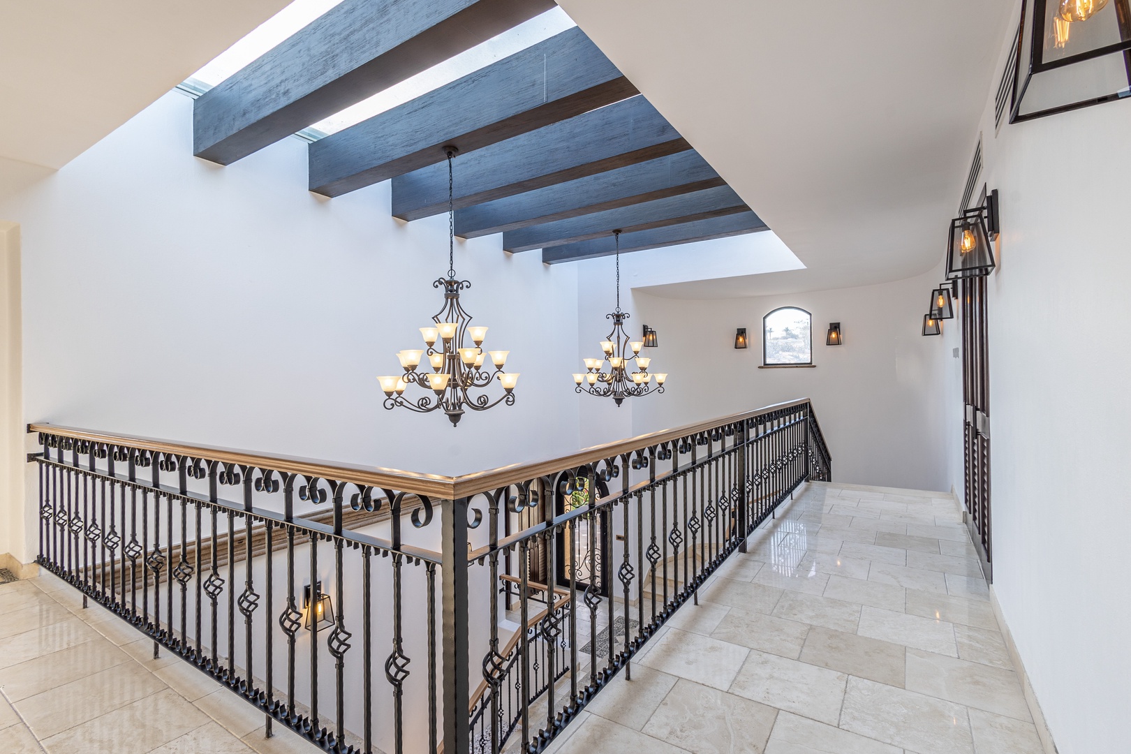 Step into soaring spaces lit by natural light streaming through striking skylights above elegant wrought-iron railings and decorative chandeliers.