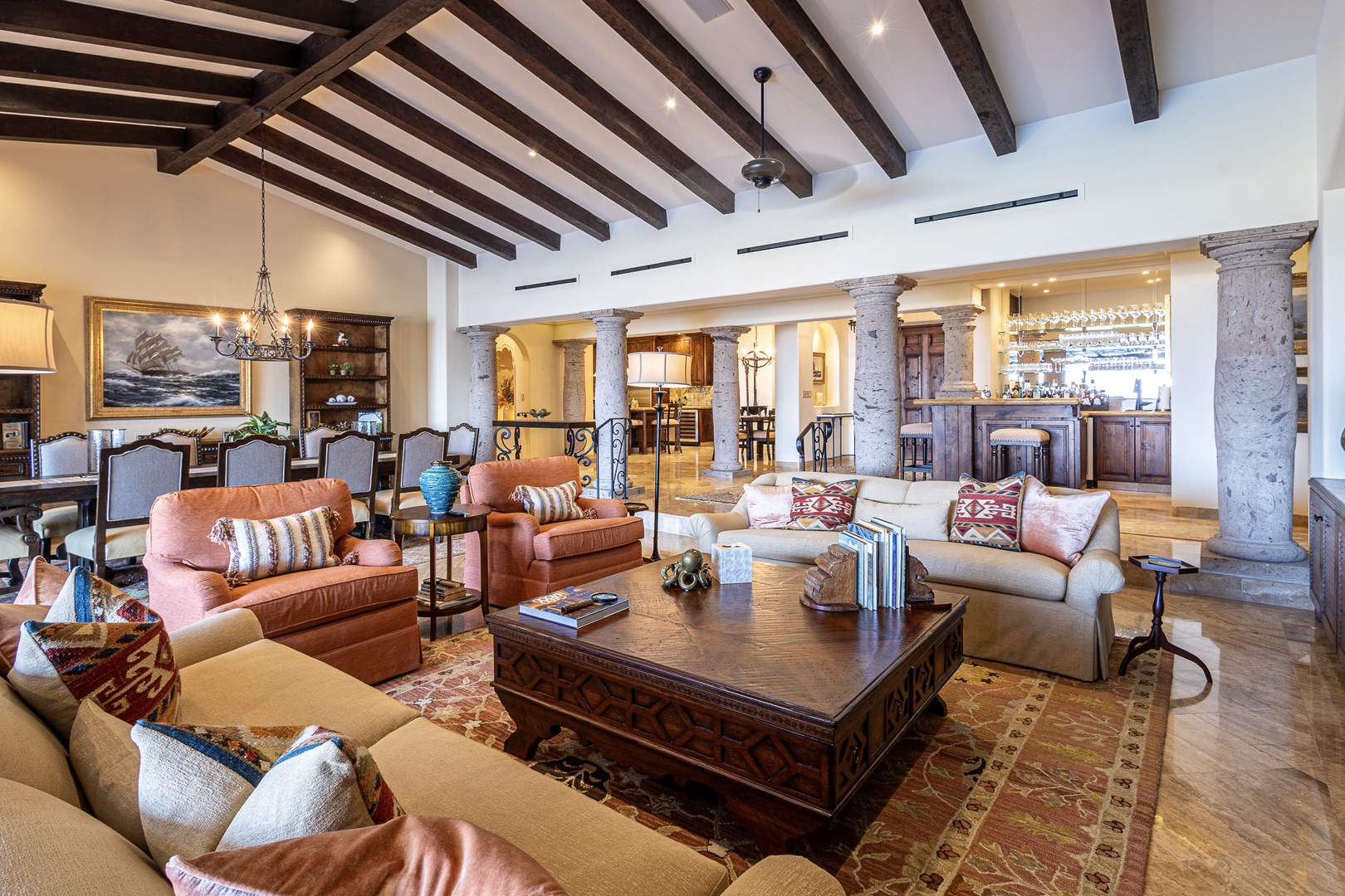Exposed wooden beams soar overhead in this spacious, inviting living area where plush leather seating beckons you to unwind by rustic columns and warm lighting.