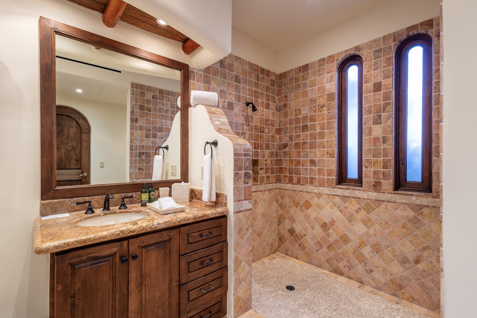 Unwind in your private spa-like bathroom, where rustic elegance meets comfort. The walk-in shower features stunning terracotta tilework, while natural light pours through arched windows, creating your perfect morning retreat.