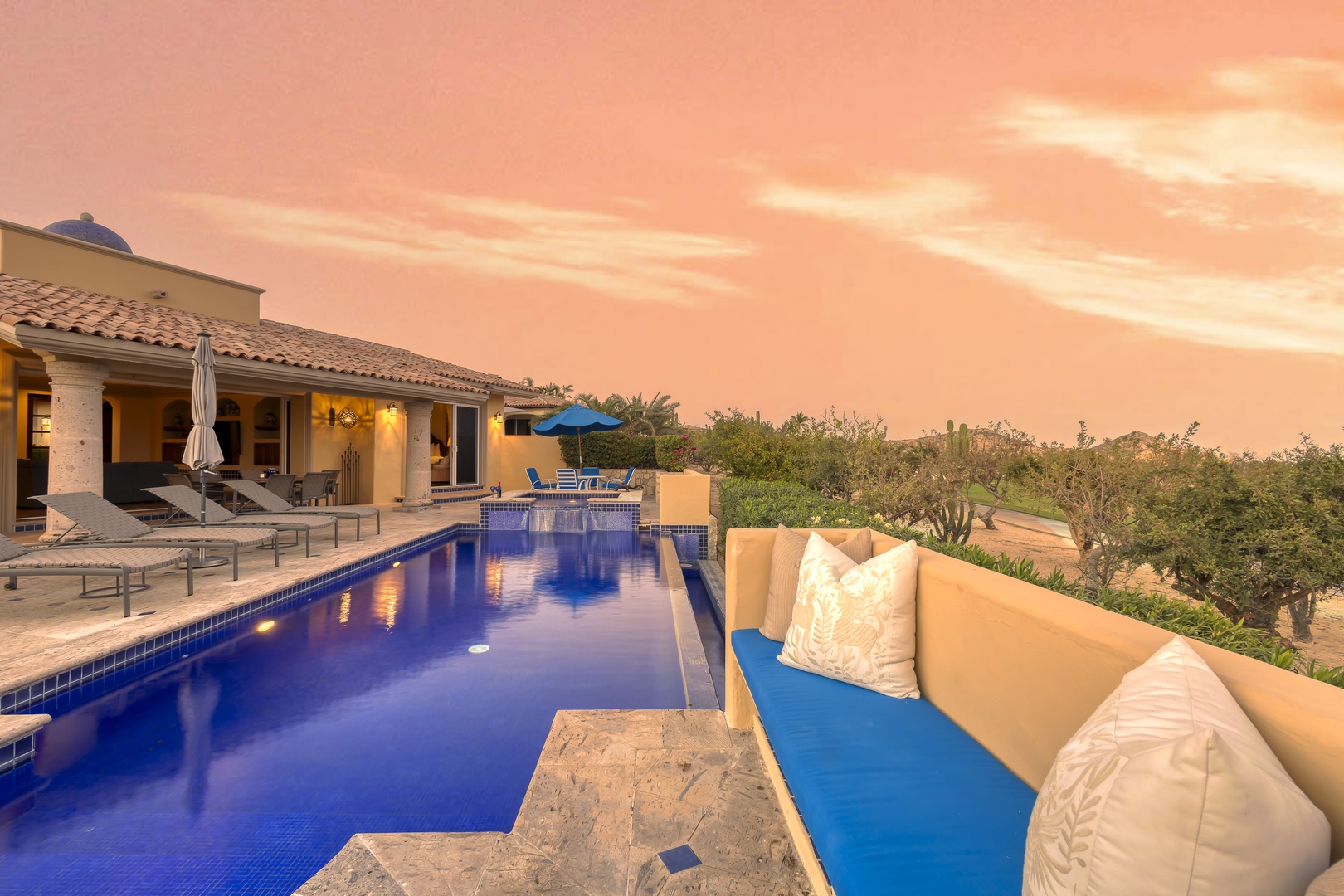 Stunning villa at golden hour with infinity pool, outdoor lounge, and dramatic desert landscape views.