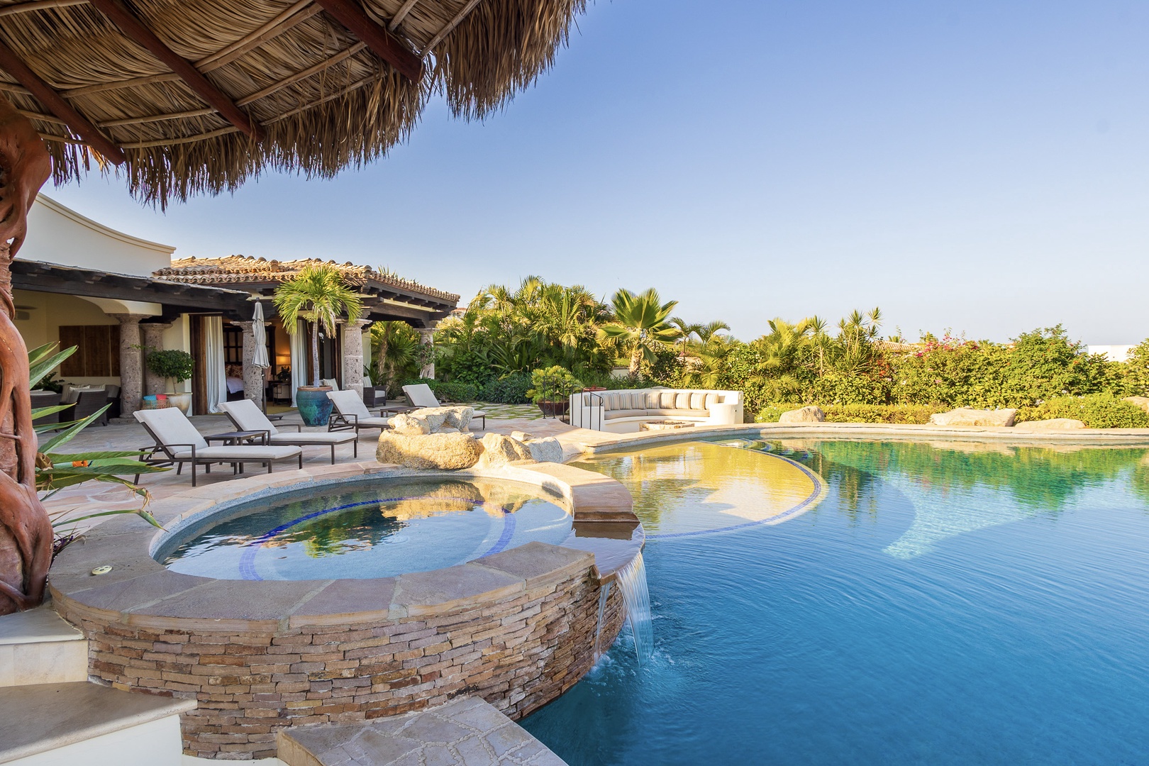 This luxurious outdoor oasis features a multi-level pool with an elevated hot tub, surrounded by loungers and lush tropical landscaping for your ultimate relaxation.