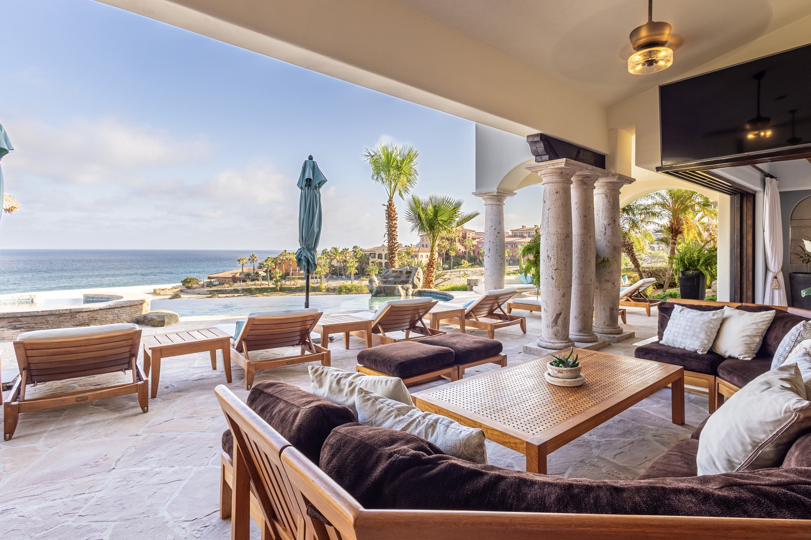 Sink into plush lounge seating and soak up stunning sea views from your private terrace, where the pool, palm trees, and coastal horizon create your perfect relaxation retreat.