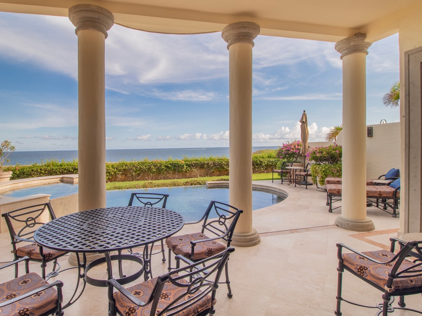 Step onto your covered terrace where elegant columns frame breathtaking ocean views. Relax by the pool with lush gardens and endless blue horizon as your backdrop.
