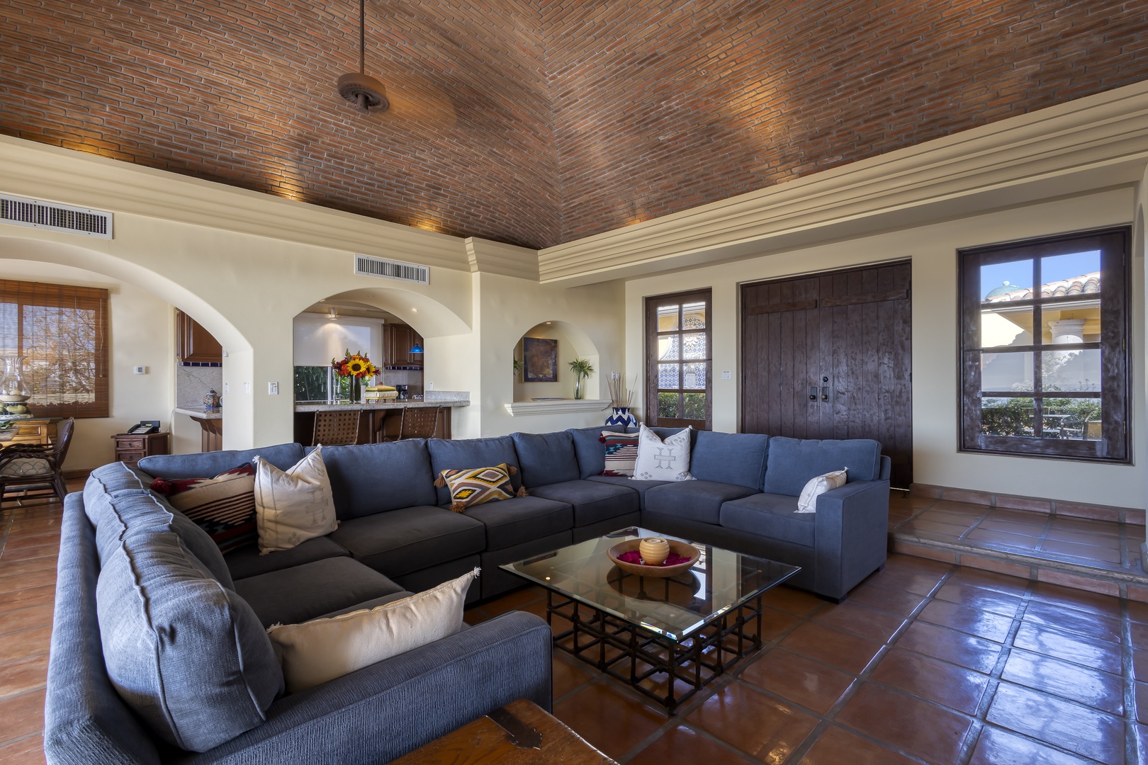 Unwind in your elegant living room featuring soaring brick ceilings, plush sectional seating, and charming arched windows that frame peaceful views.