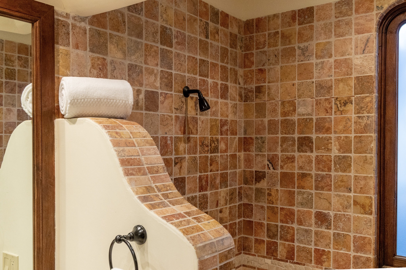 Step into your private tiled shower with warm earth-tone stone and sleek bronze fixtures—fresh towels rolled and waiting for your arrival.