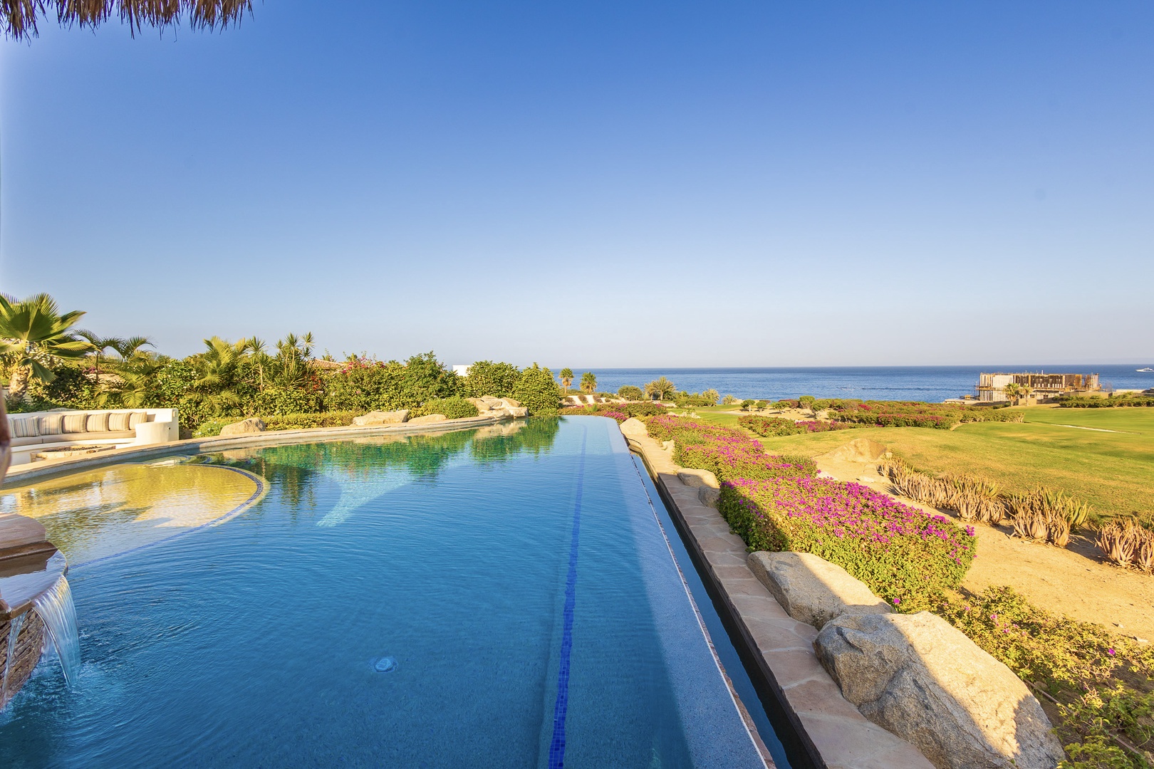 Stunning infinity pool with pristine landscaping, overlooking manicured greens and the sparkling sea beyond—a serene coastal setting for relaxation.