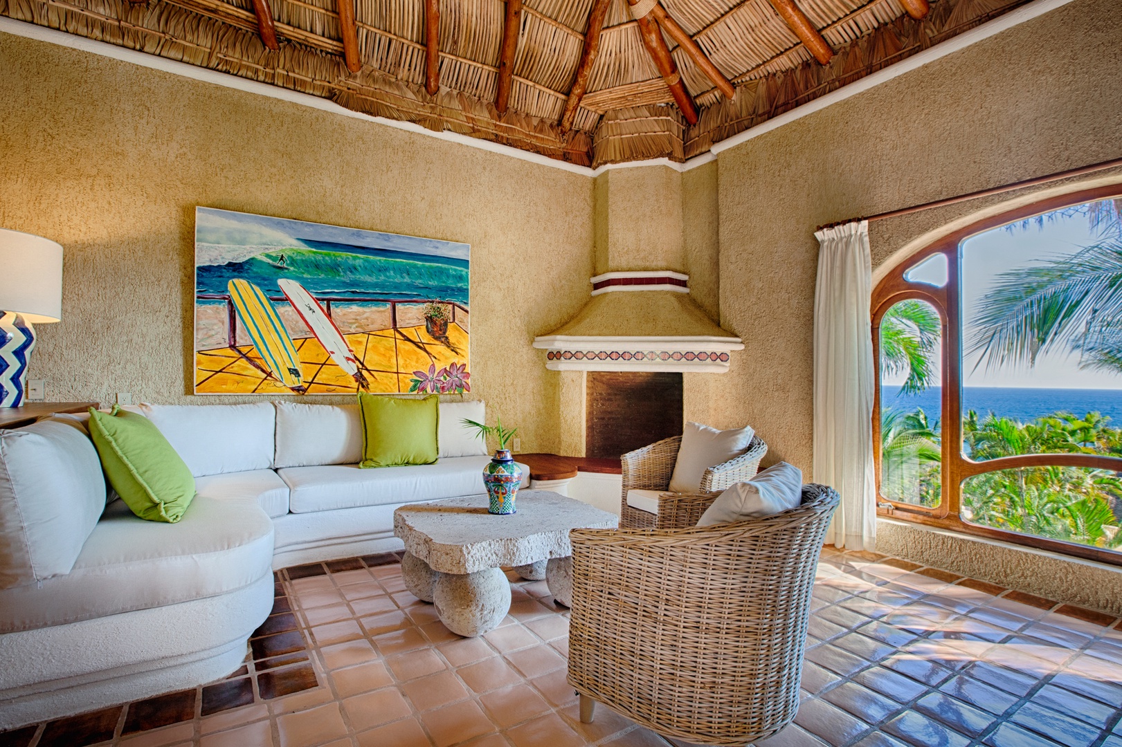 Relax in your tropical living room with authentic palapa ceiling, cozy fireplace, and ocean views through arched windows.