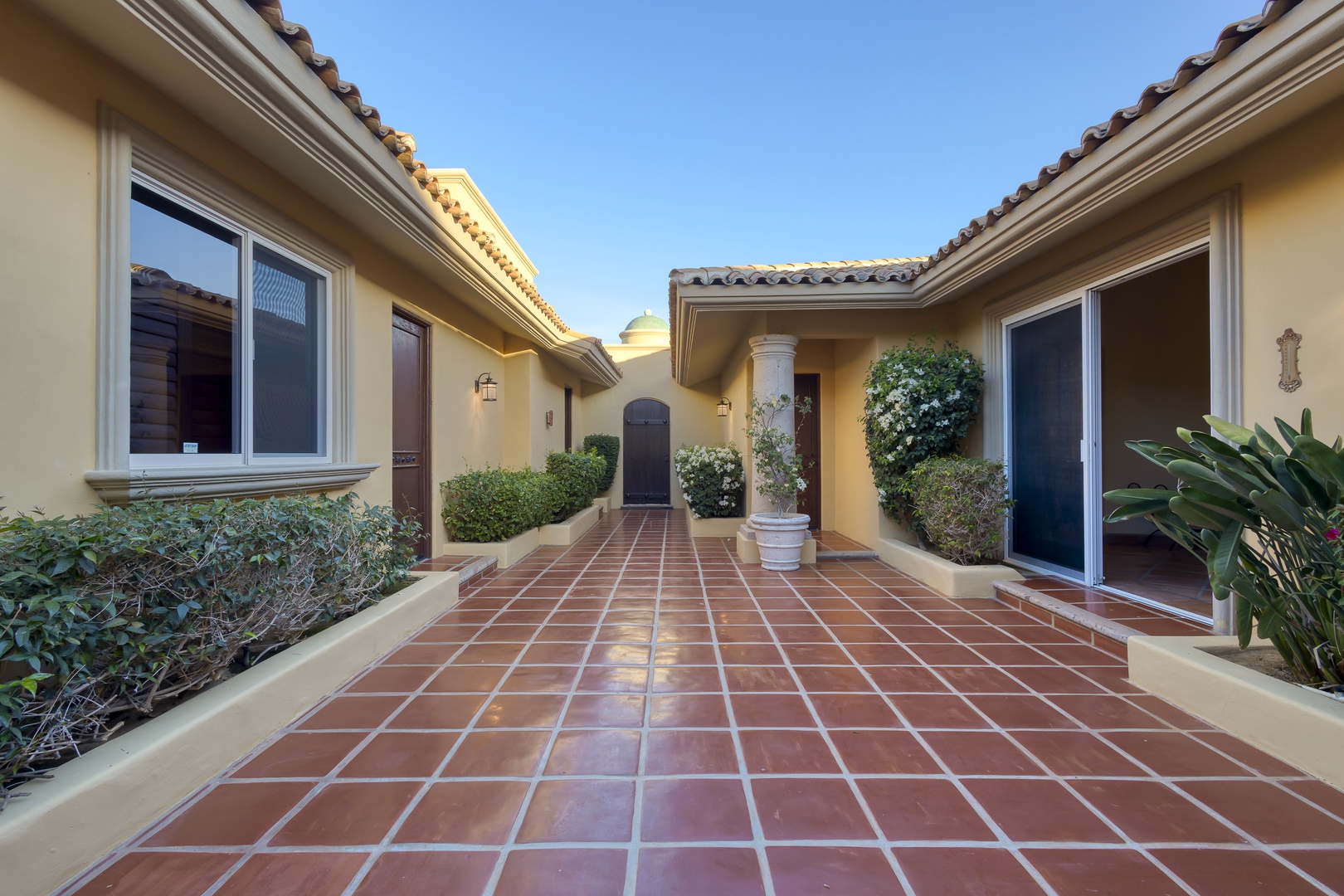 Mediterranean-style entrance courtyard with terra cotta tile flooring and manicured landscaping leading to the main entrance.