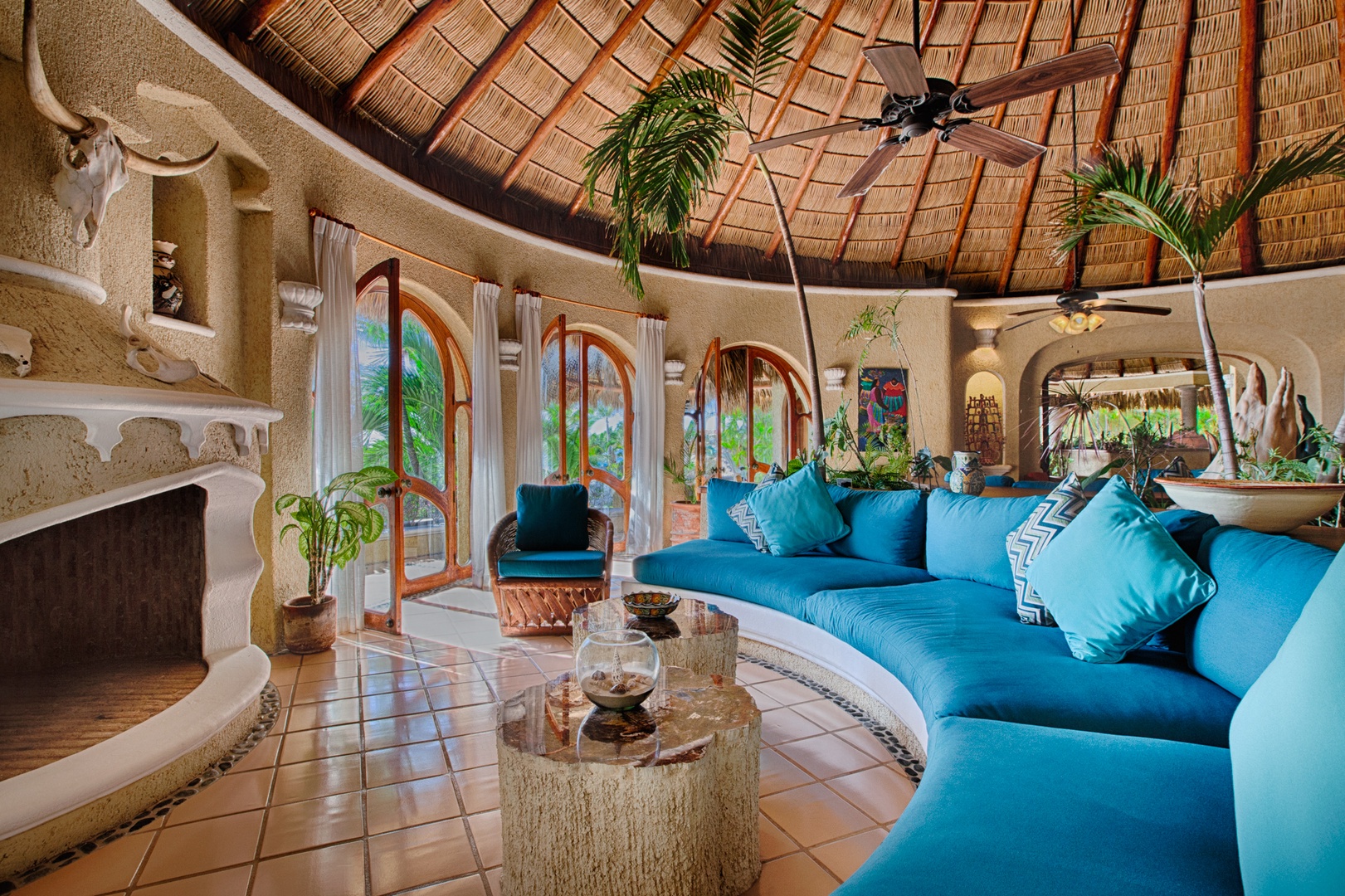 Sink into your curved blue sofa beneath the stunning palapa ceiling, where tropical breezes flow through arched windows into your serene paradise.