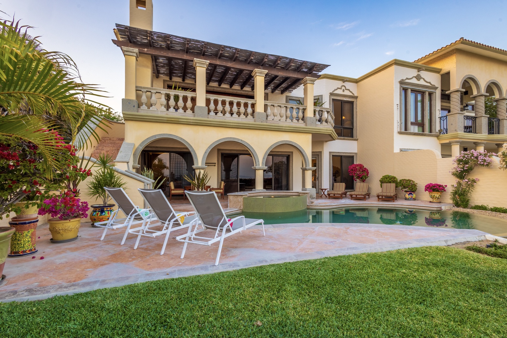 Gorgeous Mediterranean villa features a private pool, covered terrace, and lush landscaping framed by colorful blooms and tropical palms—your perfect sunny escape.