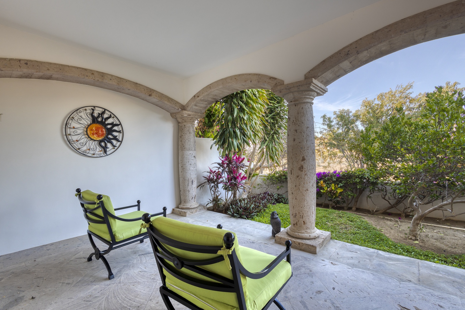 Your elegant covered terrace features vibrant lime chairs where you can unwind while admiring the lush garden views through graceful stone archways.