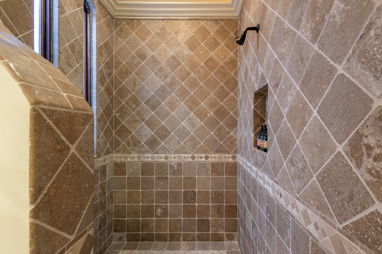 Step into your private shower oasis with elegant stone tile, overhead rainfall, and a built-in shelf for your essentials—ready to refresh you each morning.