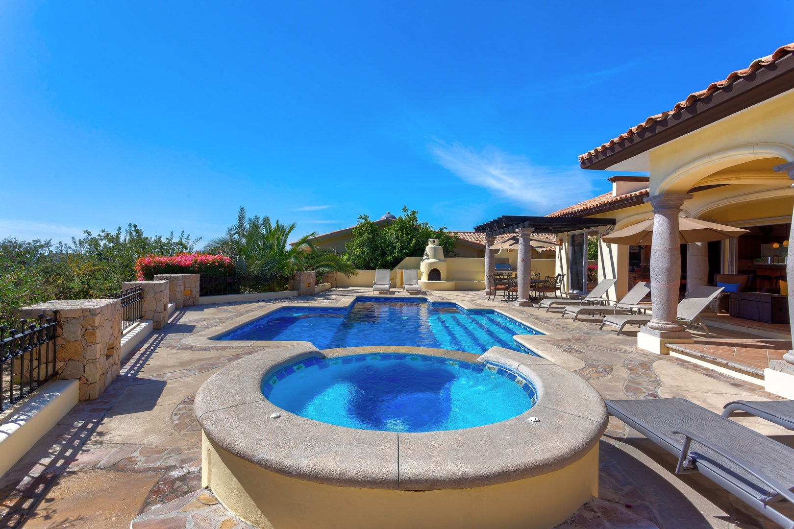 Luxurious villa features stunning pool and spa surrounded by elegant stone terraces under brilliant blue skies.