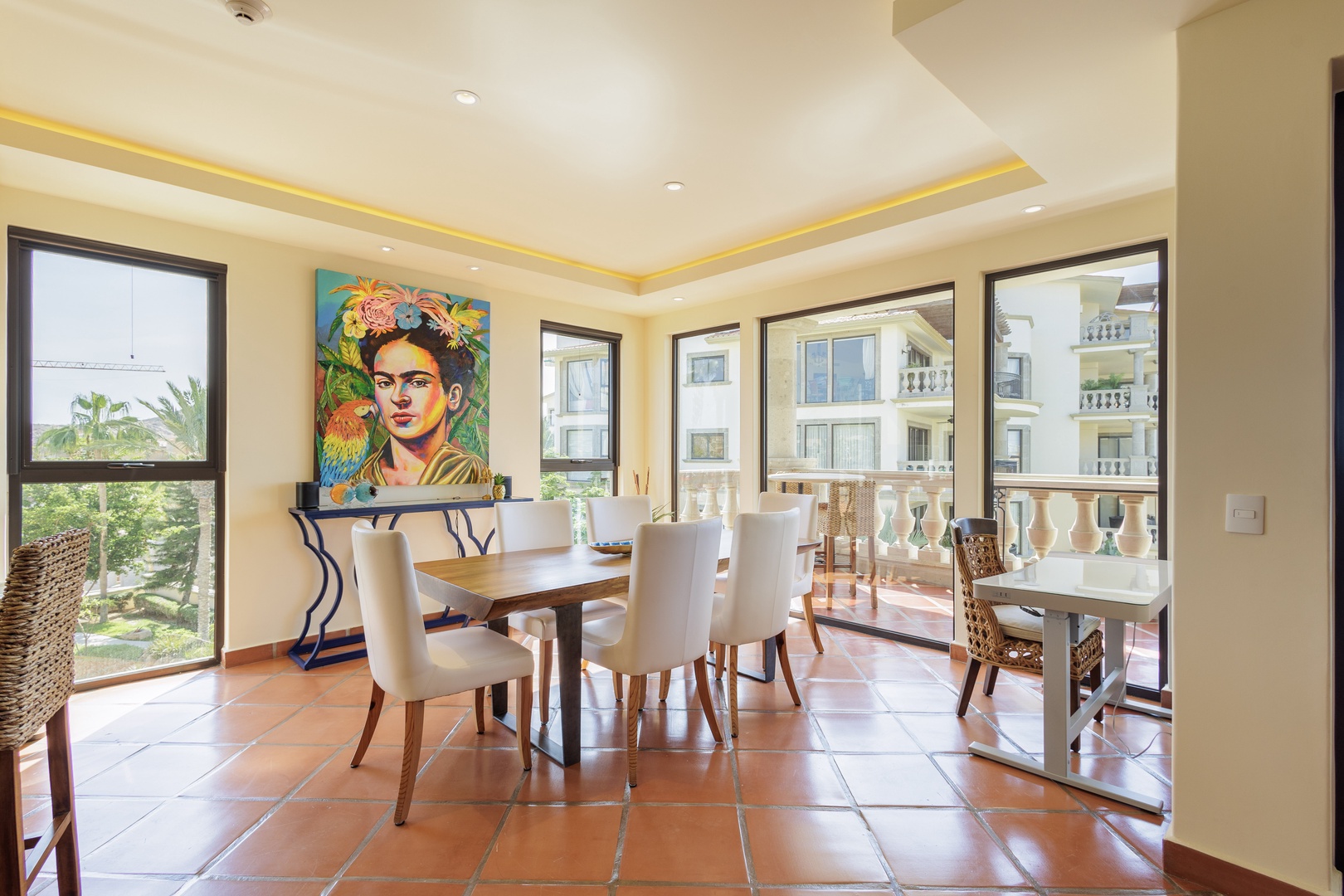 Gather around this sunlit dining table where warm terracotta tiles and vibrant art set the scene for your memorable meals together. Large windows frame garden views and invite natural light throughout your day.