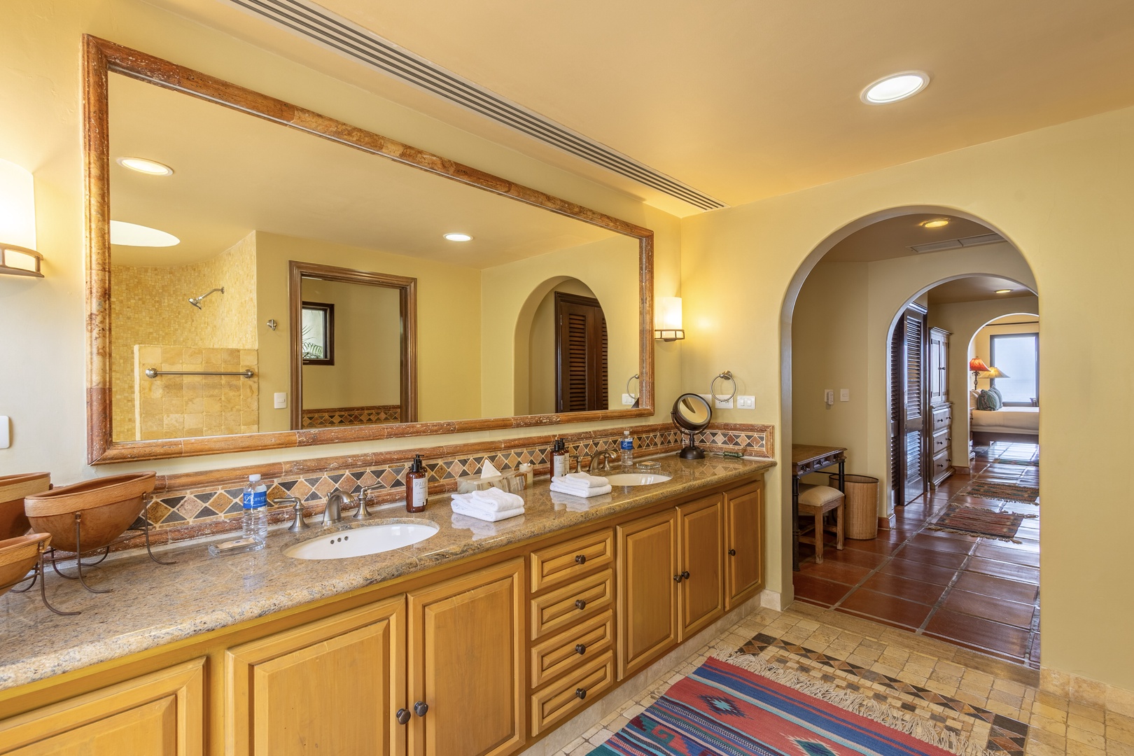 Unwind in your beautifully appointed bathroom with dual vanities, granite countertops, and warm Mediterranean-inspired tilework. Natural light spills through the archway connecting you to your peaceful retreat.