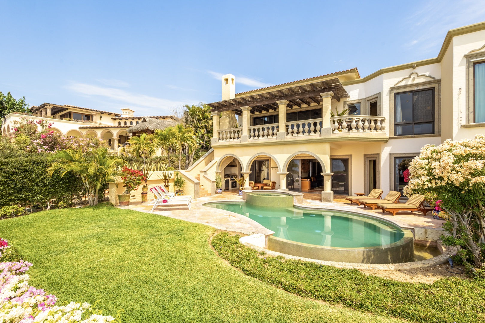 Elegant Mediterranean villa with private pool, manicured gardens, and inviting outdoor loungers set against stunning architectural arches and vibrant tropical landscaping.