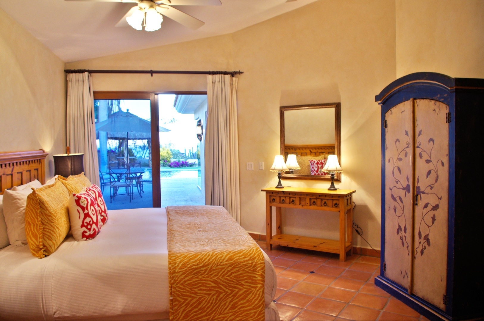 Step into your sunny sanctuary where warm terracotta tiles meet vibrant bedding and handcrafted furniture. Beyond the glass doors, your private patio awaits with poolside views and shaded seating—perfect for morning coffee or sunset cocktails.