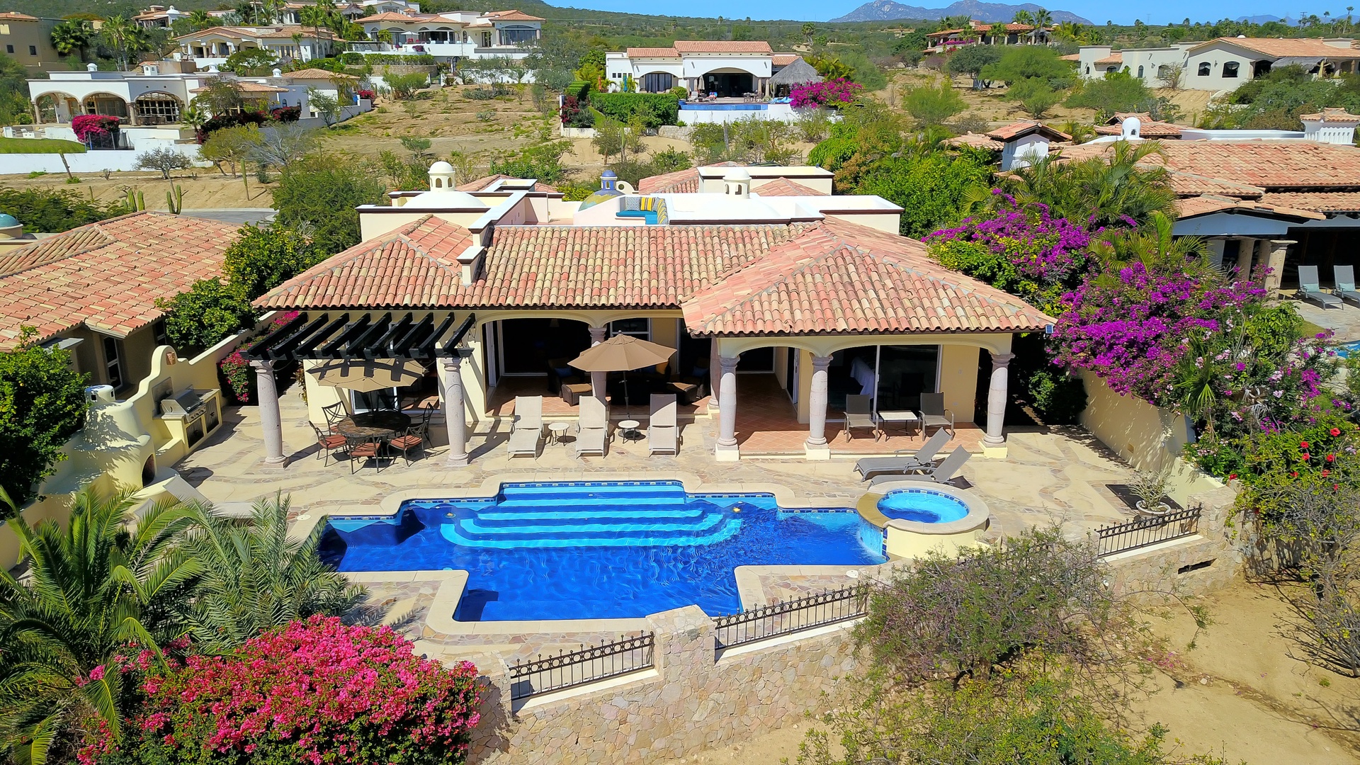 Aerial view of a luxury vacation villa featuring a stunning swimming pool, spa, and covered terrace in a beautiful hillside community.