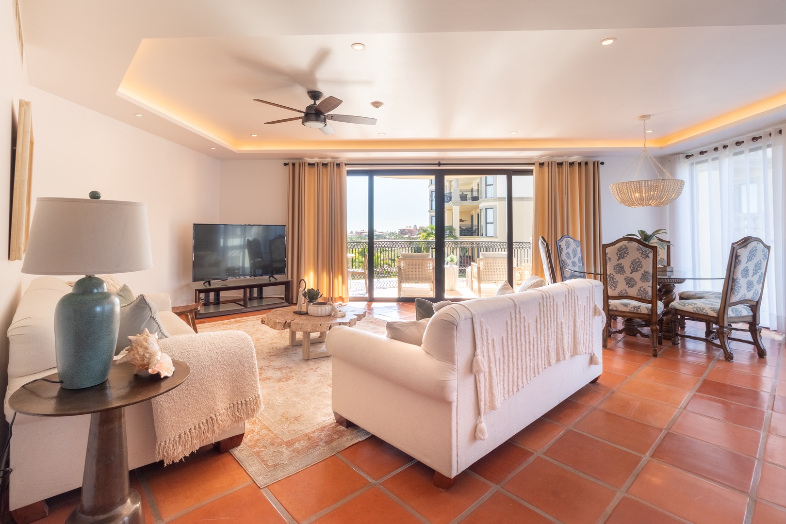 Step into your sunlit living space with warm terracotta floors, plush seating, and soft coastal accents, where glass doors open to your private balcony and inviting views beyond.