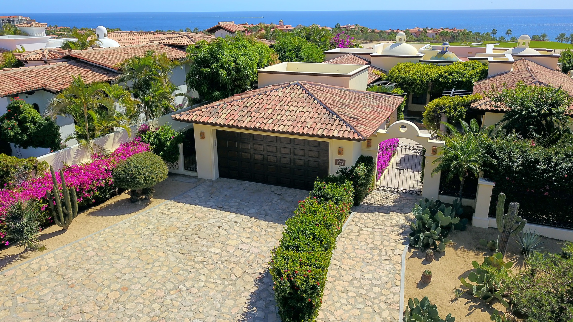 Aerial view of an elegant villa featuring clay tile roofs, private courtyard with desert landscaping, and gated entrance in an exclusive coastal neighborhood.