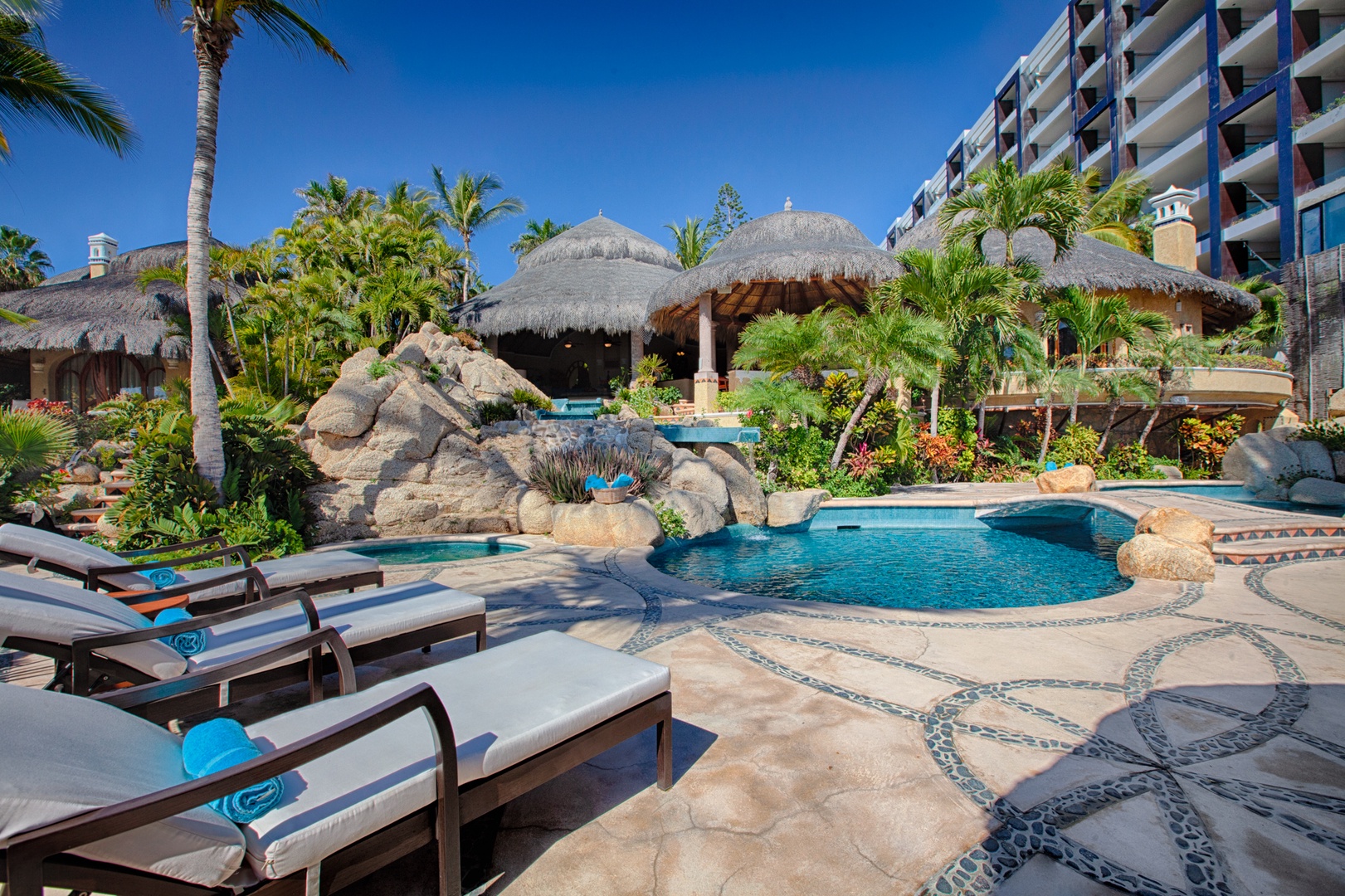 Luxurious tropical paradise with a stunning lagoon-style pool featuring natural rock formations and thatched-roof pavilions.