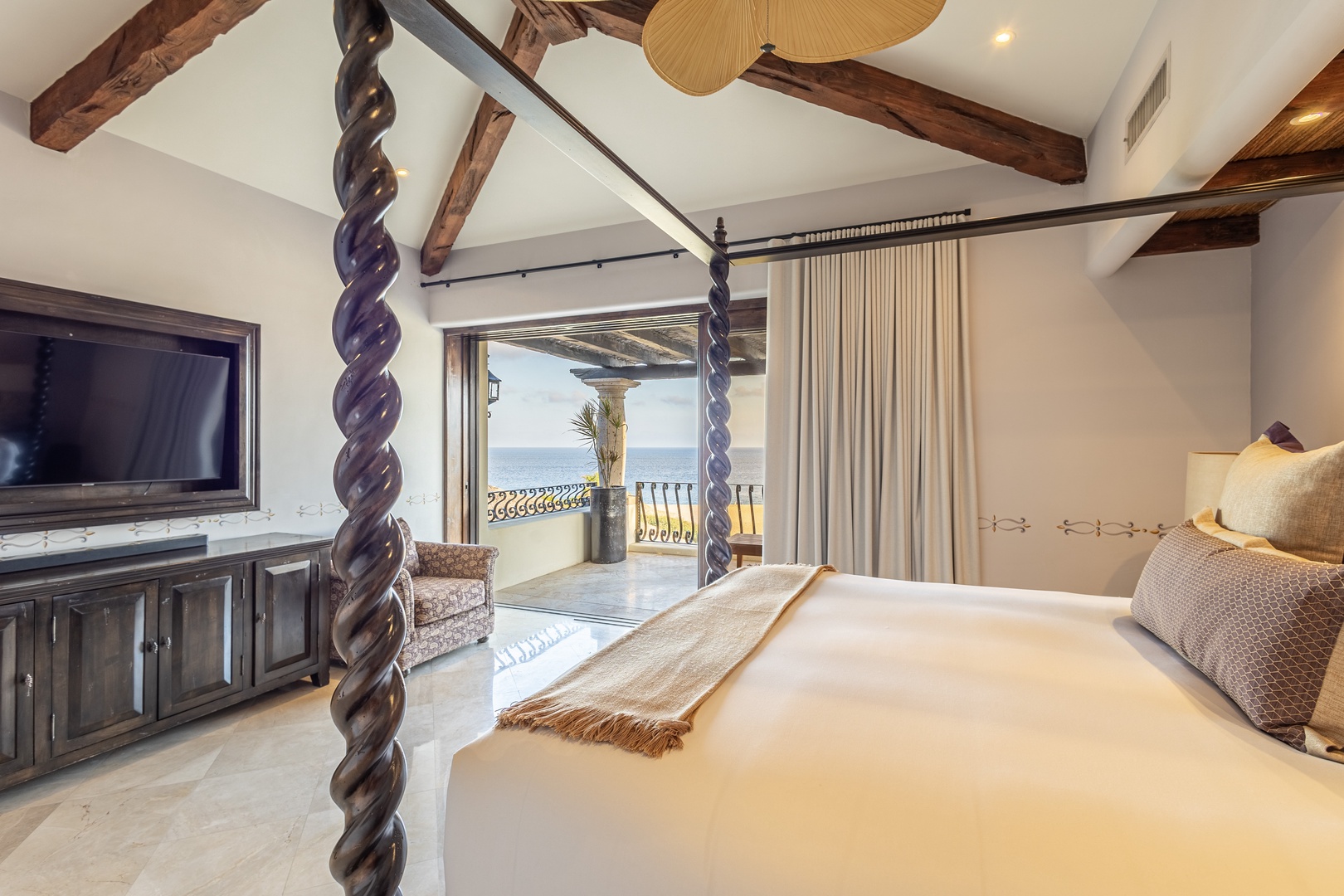 Your elegant bedroom features a hand-carved canopy bed, exposed wood beams, and a private balcony overlooking serene sea views—perfect for unwinding after a day of adventure.