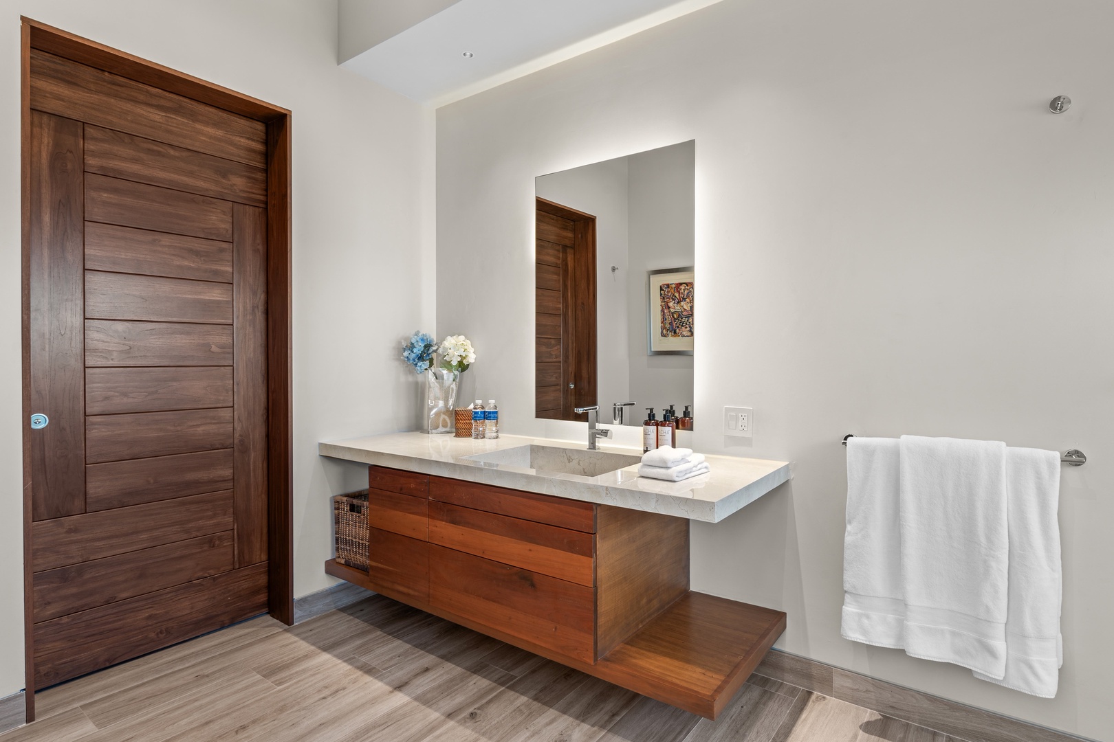 Step into your private sanctuary: a sleek, spa-like bathroom where warm wood tones meet crisp white countertops, fresh linens await, and natural light fills the space.
