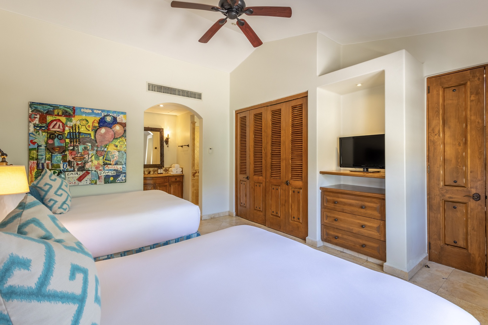 Sleep soundly in your twin-bed room featuring warm wood furnishings, vibrant artwork, and modern amenities including AC and flat-screen TV for ultimate comfort.
