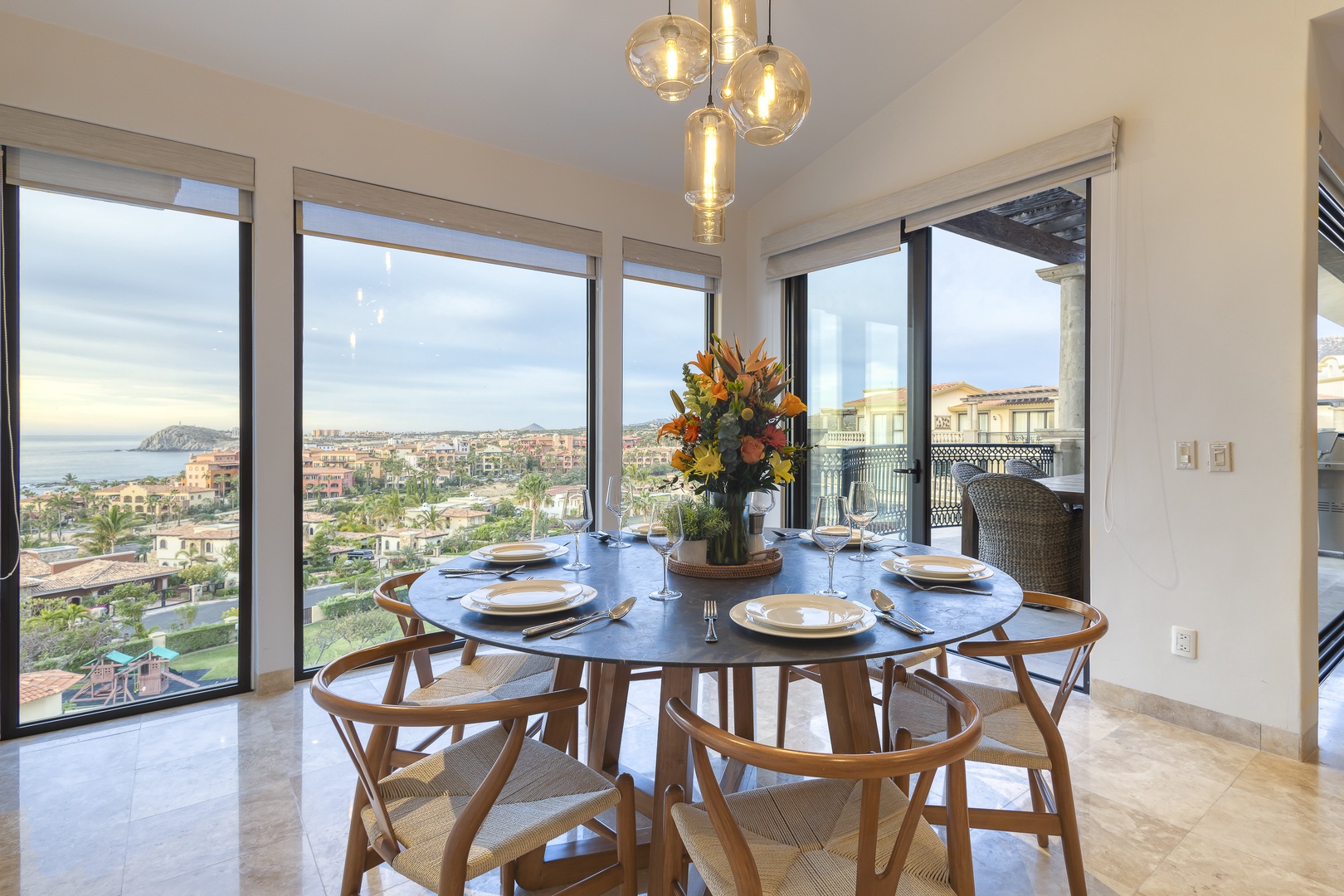 Gather around this elegant dining table and savor meals with stunning coastal and city views framing every moment. The warm pendant lighting and panoramic windows create an inviting atmosphere for your memorable evenings.