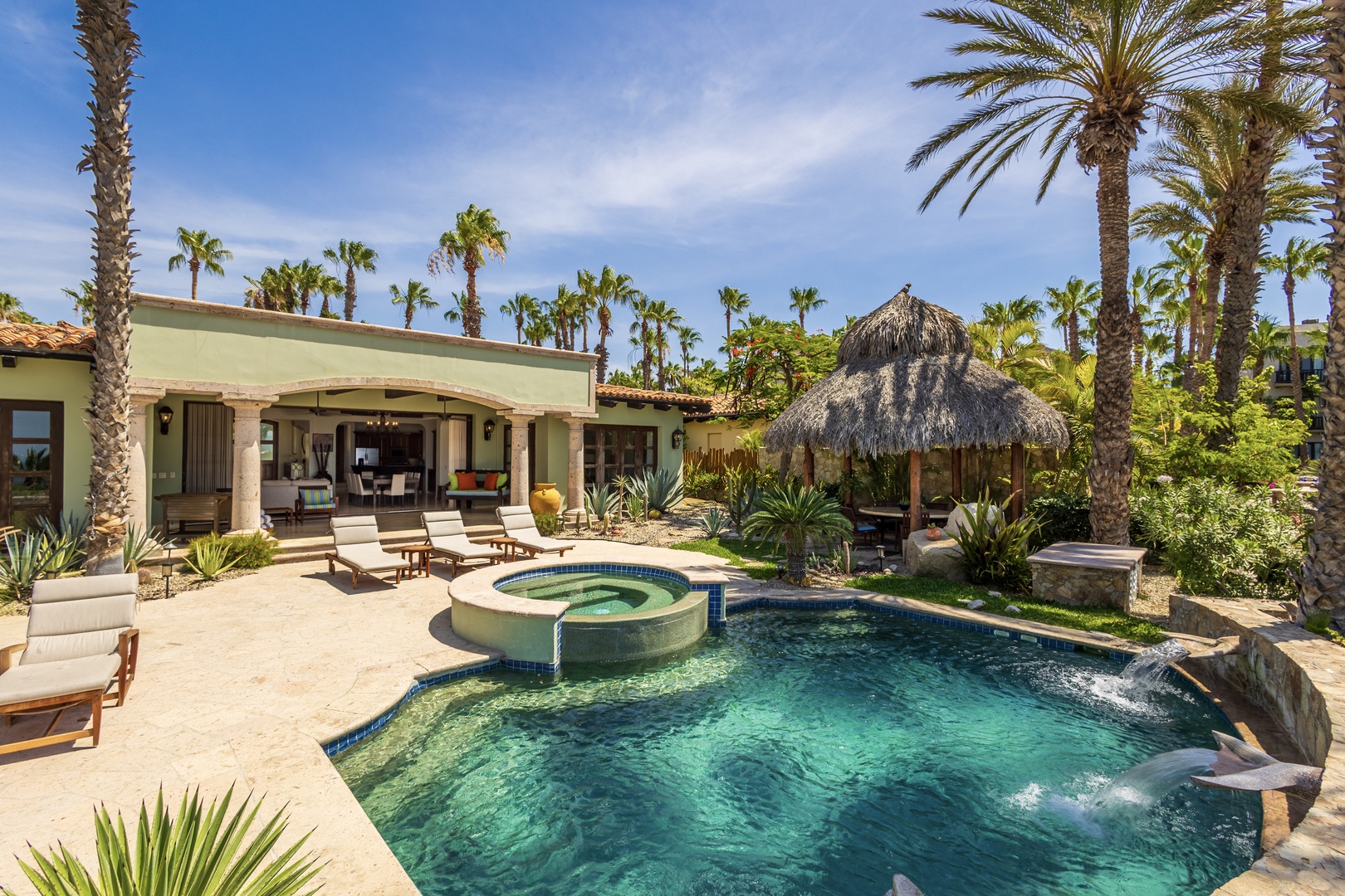 A luxurious tropical oasis awaits, with a sparkling pool, bubbling hot tub, and thatched palapa nestled among swaying palms and lush gardens—your private paradise for sun-soaked relaxation.