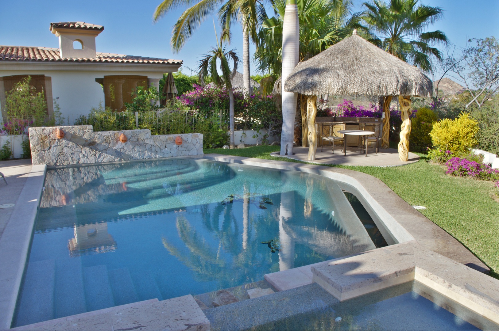 Dive into crystal-clear waters surrounded by swaying palms and vibrant blooms. Your private pool awaits, with a thatched palapa for shaded lounging and lush gardens framing your tropical retreat.
