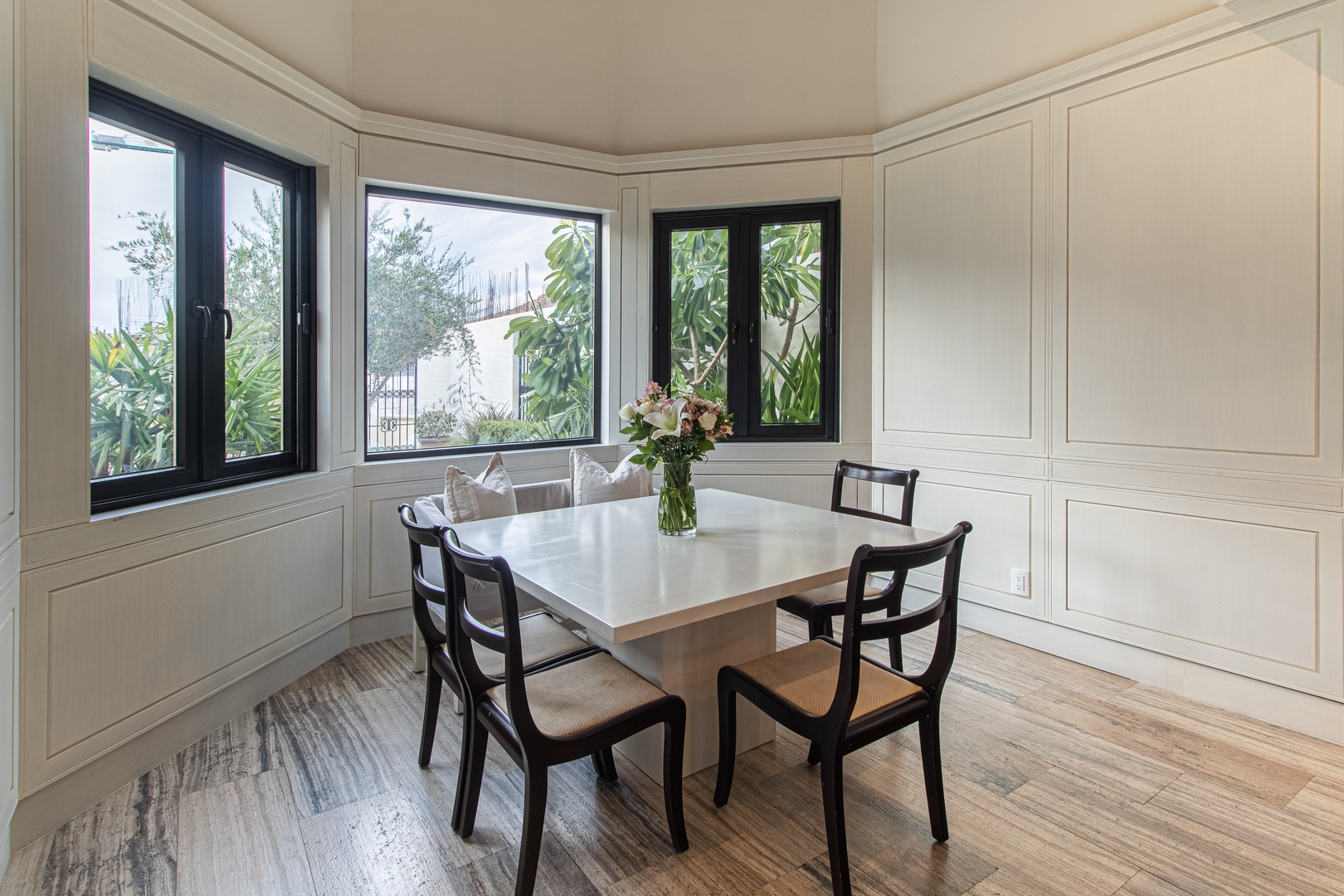 Gather for meals in this elegant dining nook, where natural light frames lush garden views through black-framed windows. The hardwood floors and crisp white paneling create a bright, welcoming atmosphere for your morning coffee or evening dinners.