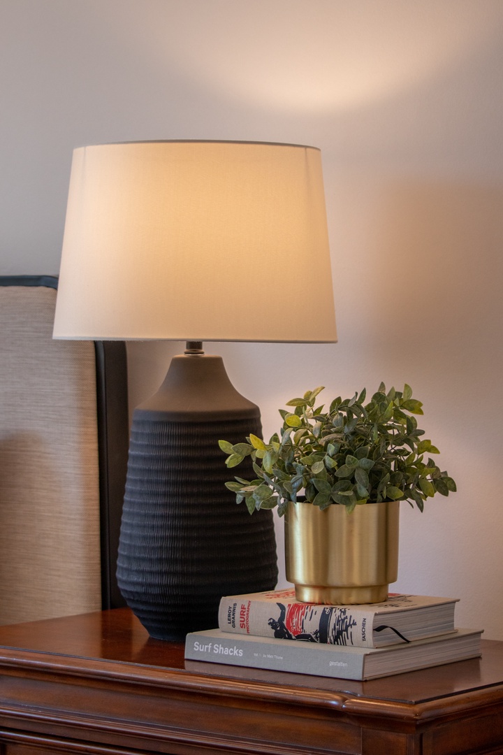 Your bedside comes alive with warm ambient lighting, fresh greenery in a modern brass planter, and curated reading material—every detail designed for your comfort and relaxation.