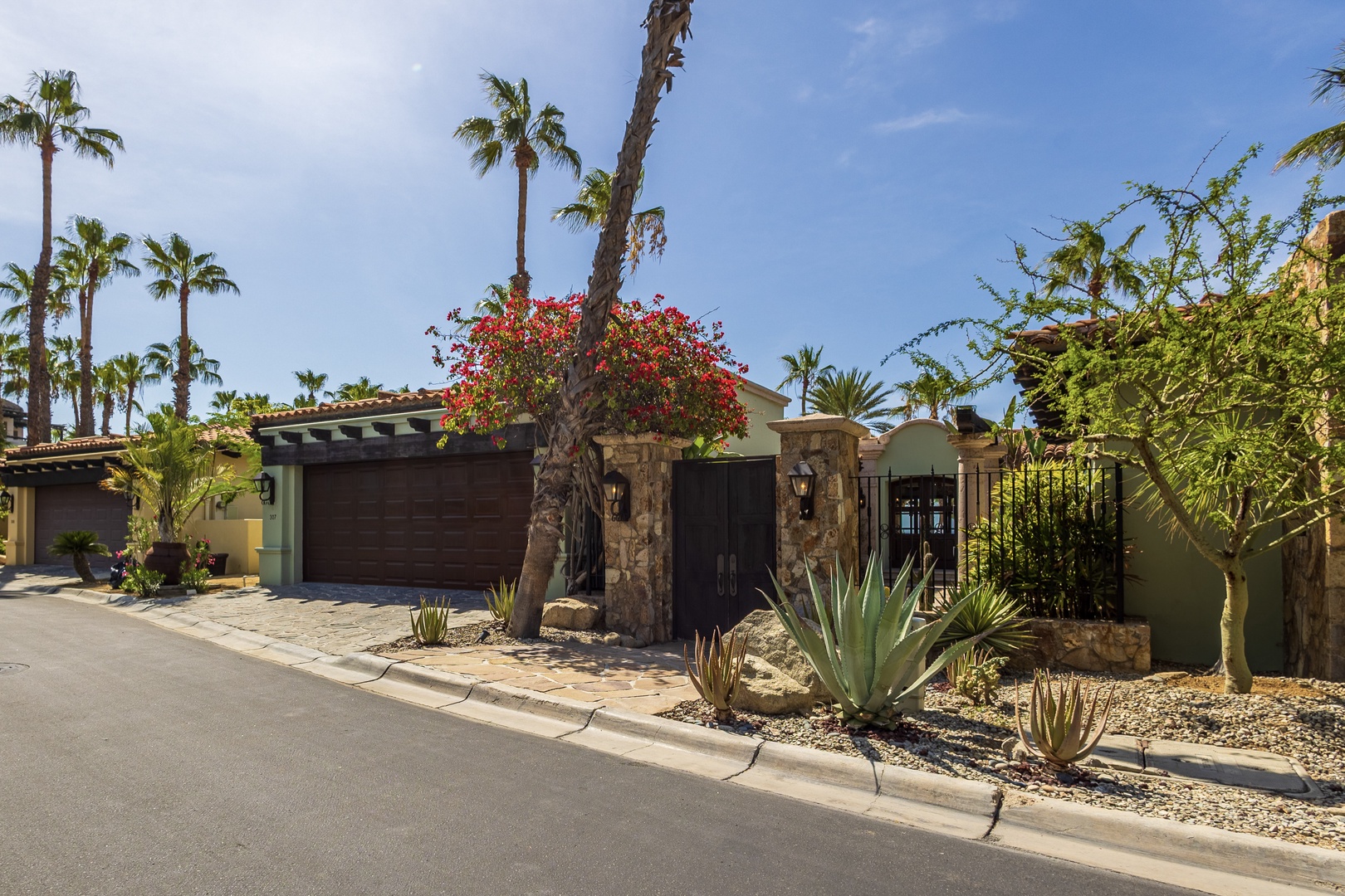 Stunning desert oasis property featuring stone pillars, tropical palms, and vibrant bougainvillea creating an elegant arrival experience.