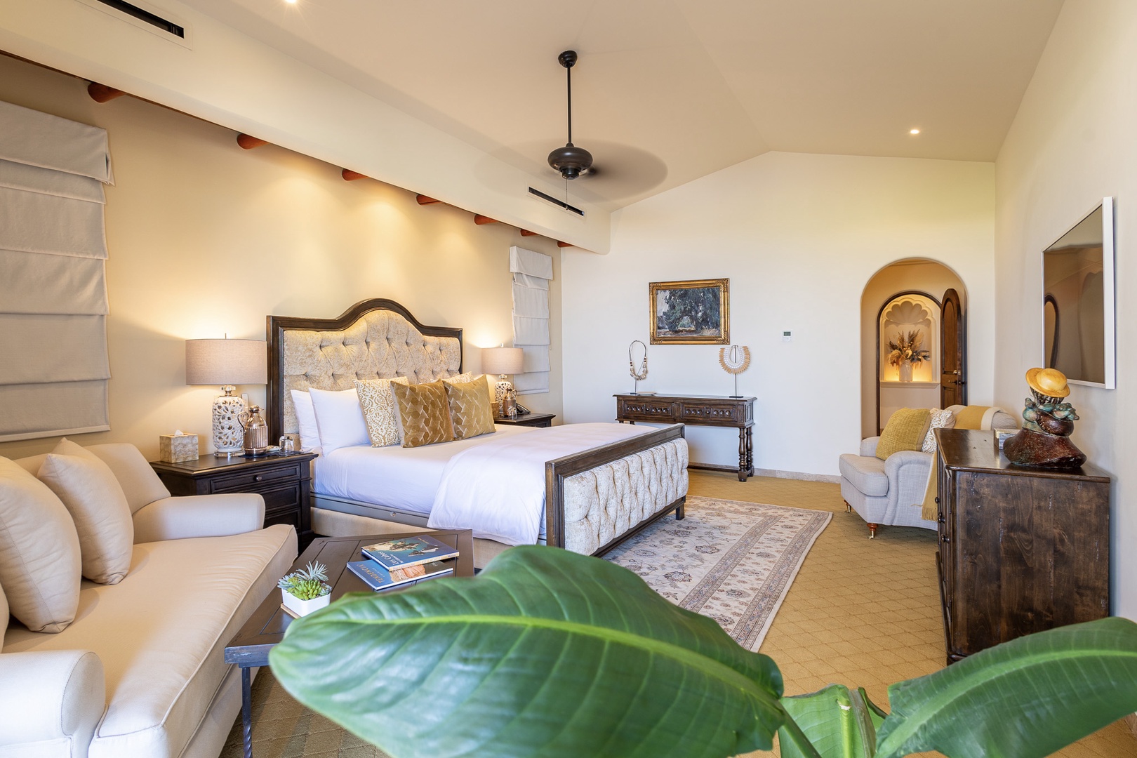 Unwind in your elegantly appointed bedroom where luxurious linens, thoughtful furnishings, and soft lighting invite restful evenings. A plush seating area and archways framing golden light create a serene retreat for your stay.