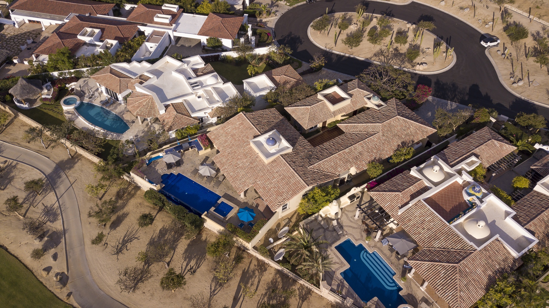 Aerial view of an upscale residential community featuring Mediterranean-style homes with clay tile roofs and private swimming pools.