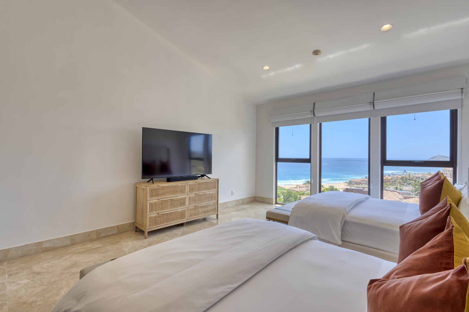 Wake up to stunning ocean views framed by floor-to-ceiling windows. Your bright, modern bedroom features two plush beds, a flat-screen TV, and serene coastal vibes inviting you to unwind in paradise.