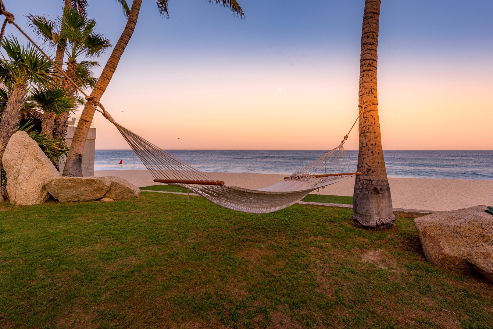 A hammock strung between swaying palms overlooks golden sands and tranquil ocean waters at sunset, offering a peaceful beachfront escape at the property.