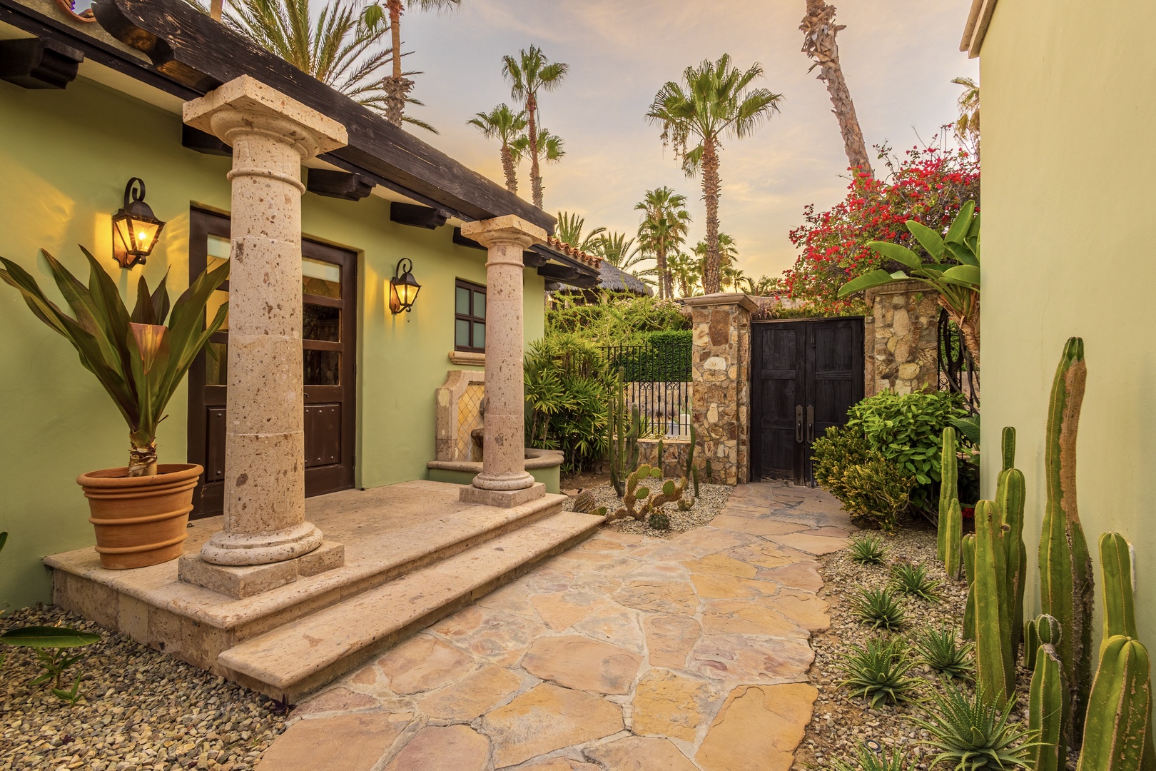 A tranquil entrance courtyard with stone columns, lush tropical palms, and vibrant desert plantings welcomes you to this southwestern-style retreat.