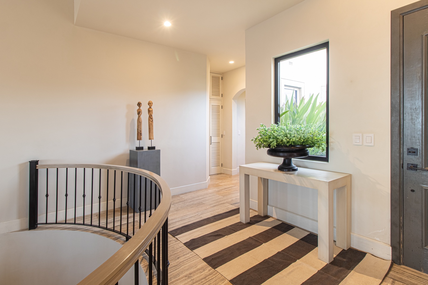 Step into a bright, elegant hallway where natural light and coastal charm welcome you. The large window frames greenery outside, and warm wood floors invite you to explore your vacation retreat.