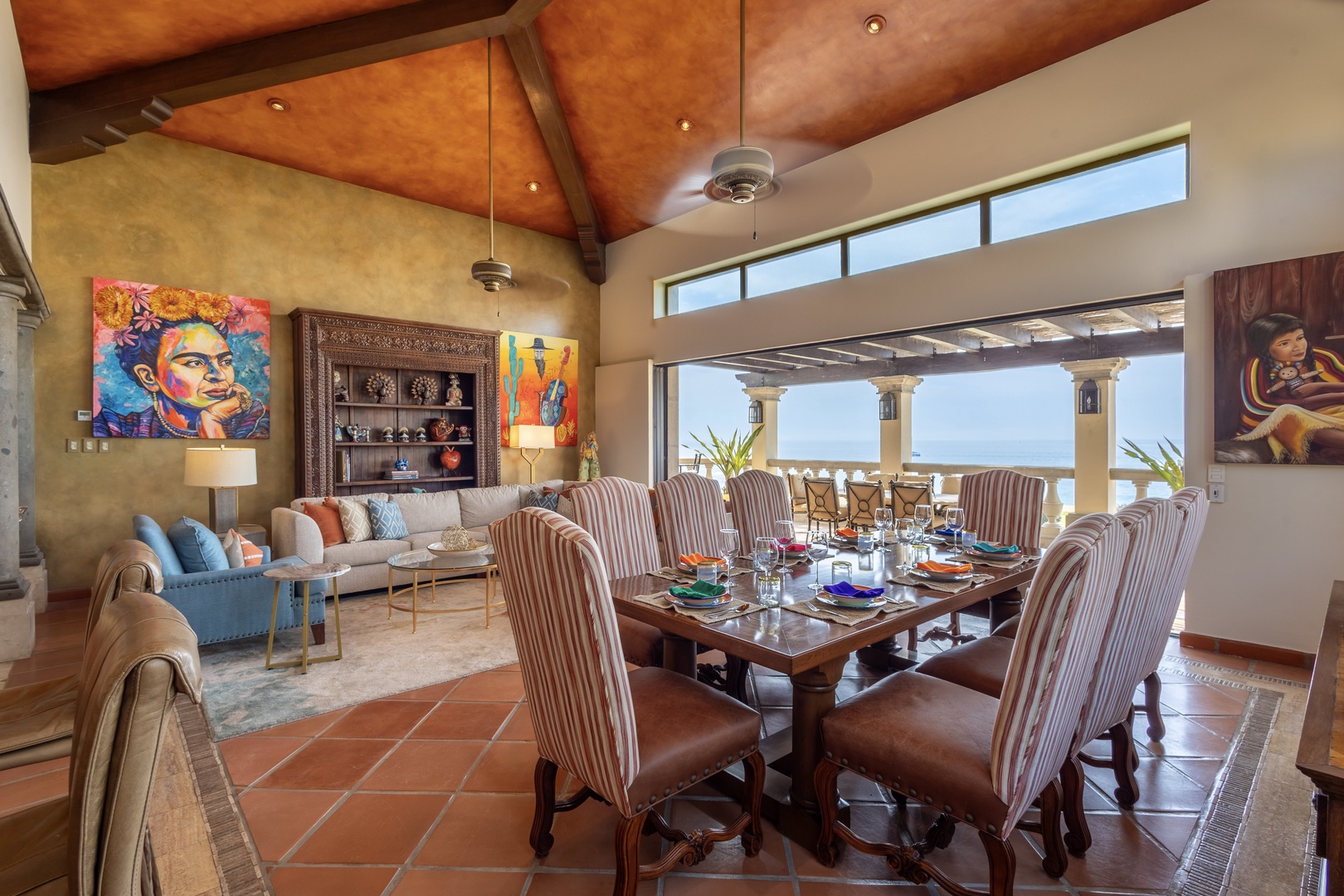Gather around the elegantly set dining table beneath soaring wood ceilings, where vibrant art and ocean views create the perfect backdrop for your memorable meals together.