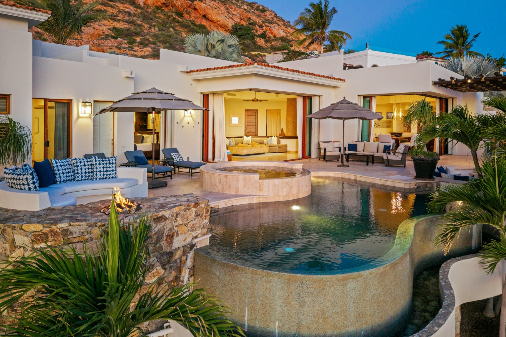 Luxurious beachfront villa with infinity pool, tropical landscaping, and dramatic mountain backdrop creating the perfect sunset setting.
