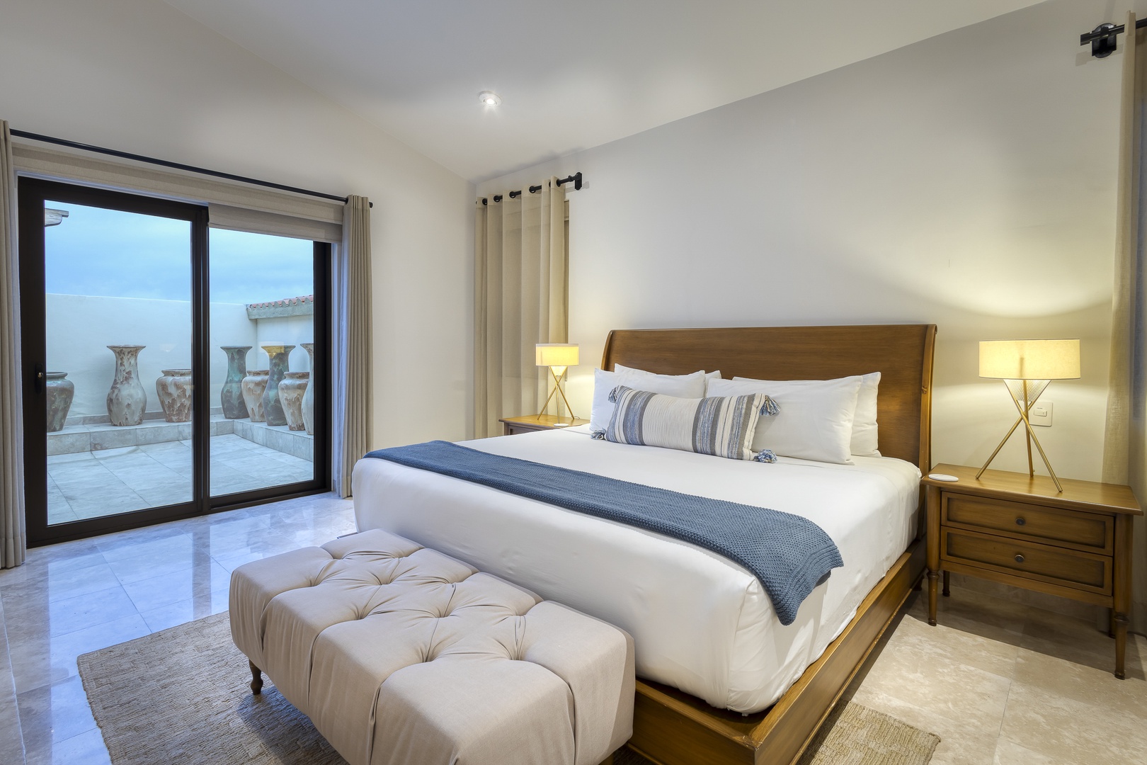 Unwind in your elegantly designed bedroom with plush bedding, warm lighting, and your own private terrace overlooking serene Mediterranean-inspired urns and coastal views.