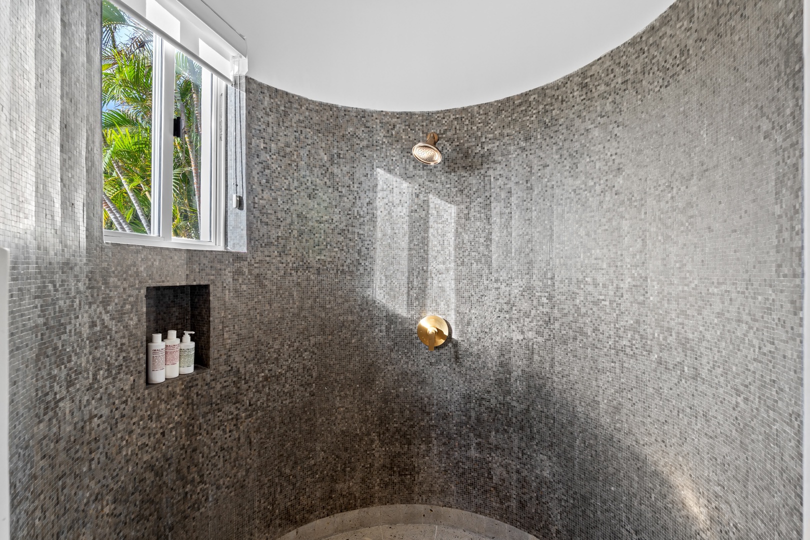 Step into your luxurious spa-style shower featuring stunning mosaic tiles and tropical garden views through elegant windows.