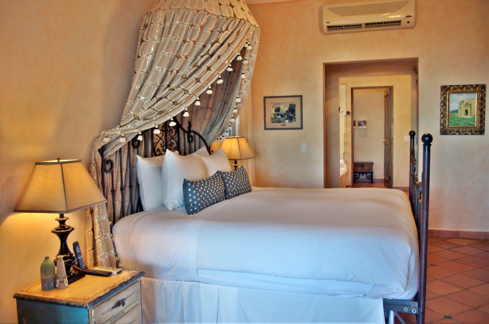 Sink into plush bedding under an elegant draped canopy, where warm lighting and artful touches create your peaceful retreat. Your ensuite bathroom awaits through the doorway.