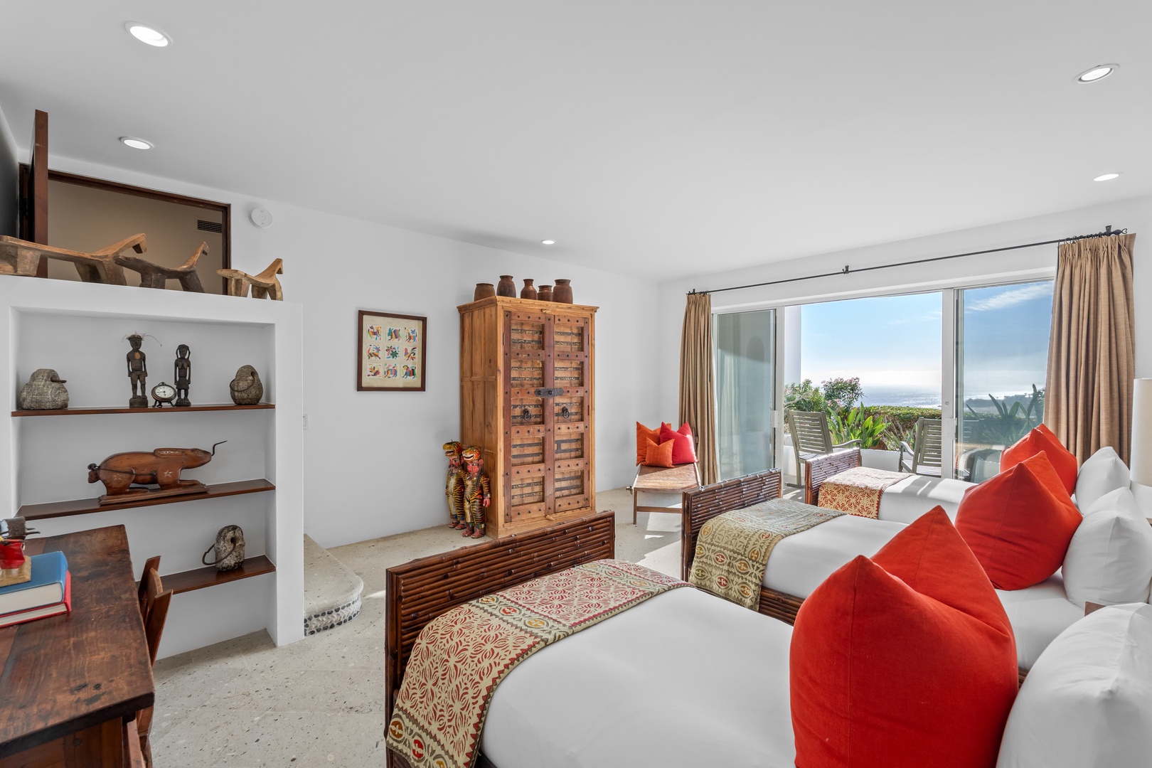 Relax in your beautifully appointed bedroom featuring vibrant red pillows, authentic artwork, and sliding doors opening to your private terrace with garden views.