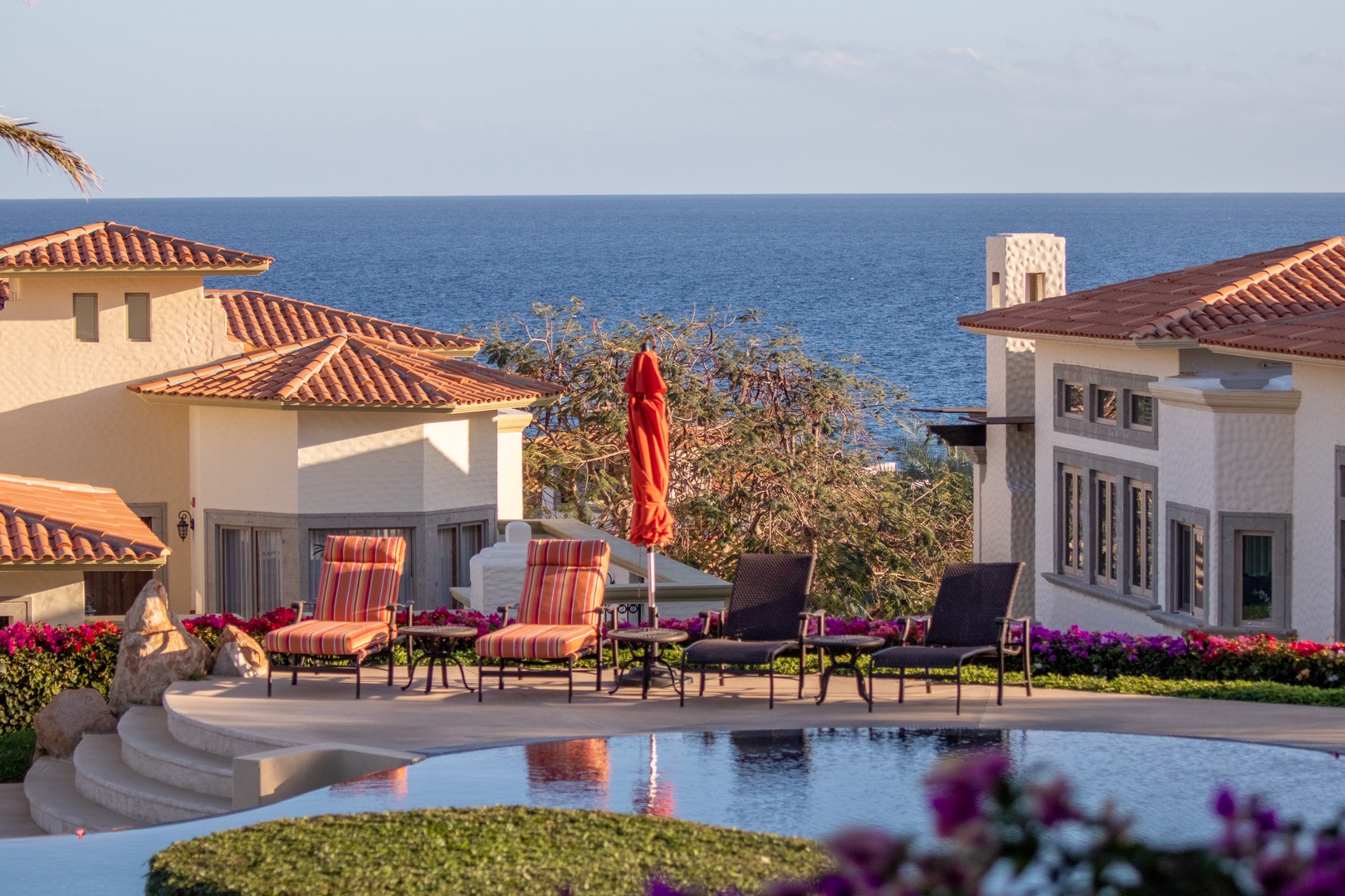 Mediterranean-style villas with private pool, sea views, and lush gardens framed by colorful bougainvillea and palm trees in a tranquil coastal setting.