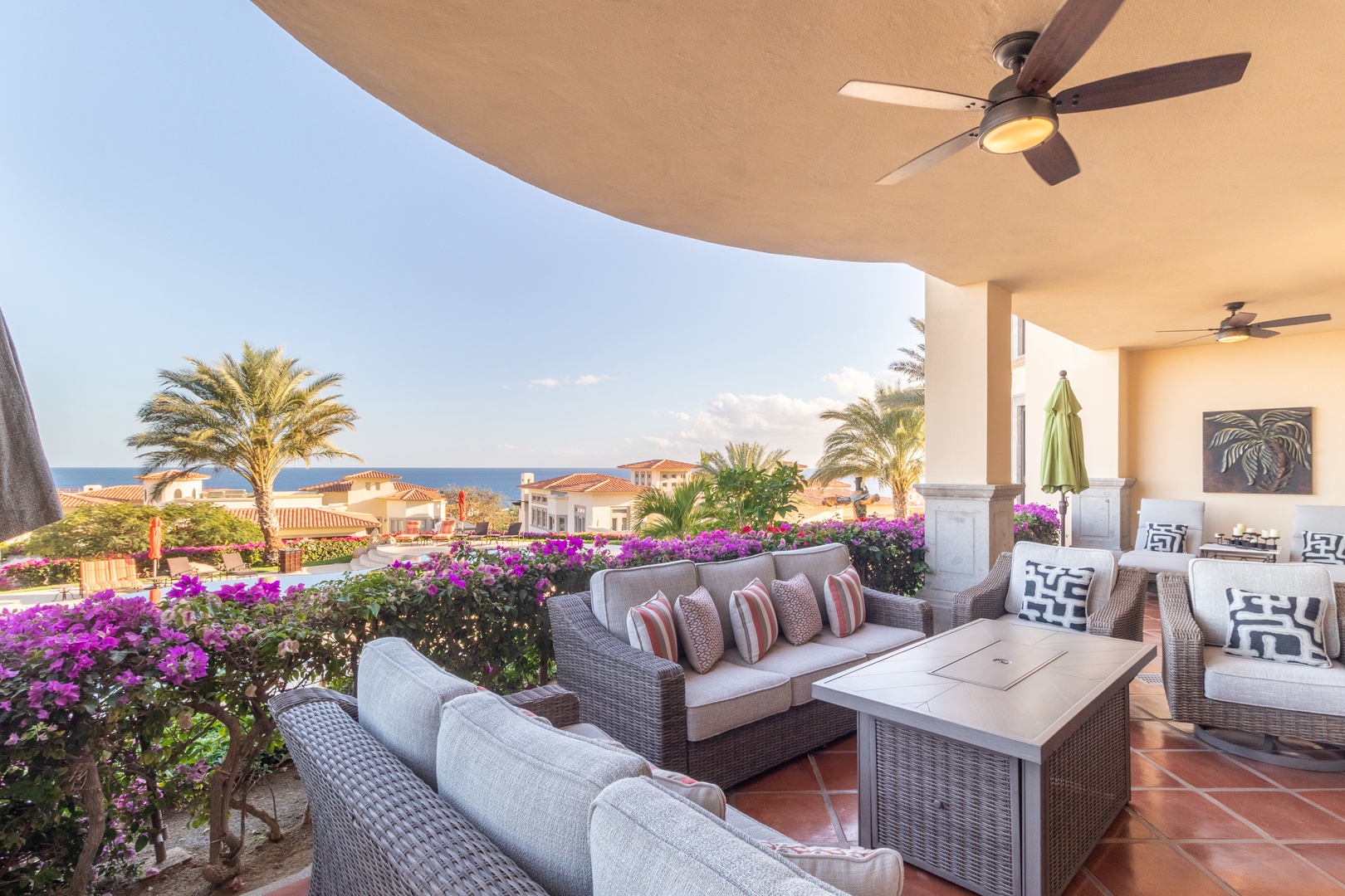 Covered terrace with wicker seating overlooking vibrant bougainvillea, swaying palms, and panoramic ocean views—a serene spot for morning coffee or sunset cocktails.
